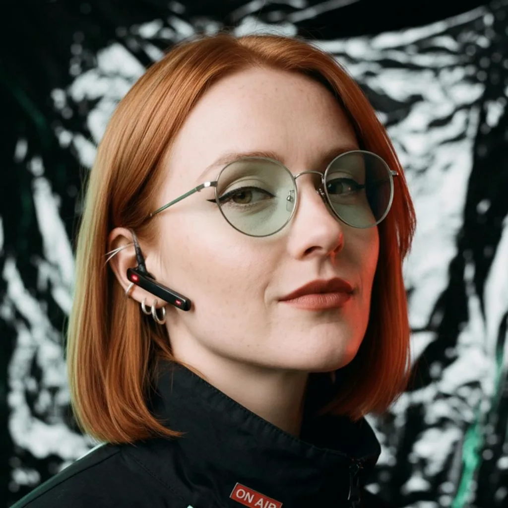 Margot, an AI-generated character: copper-red bob, round mint-tinted glasses, black high-collar jacket.